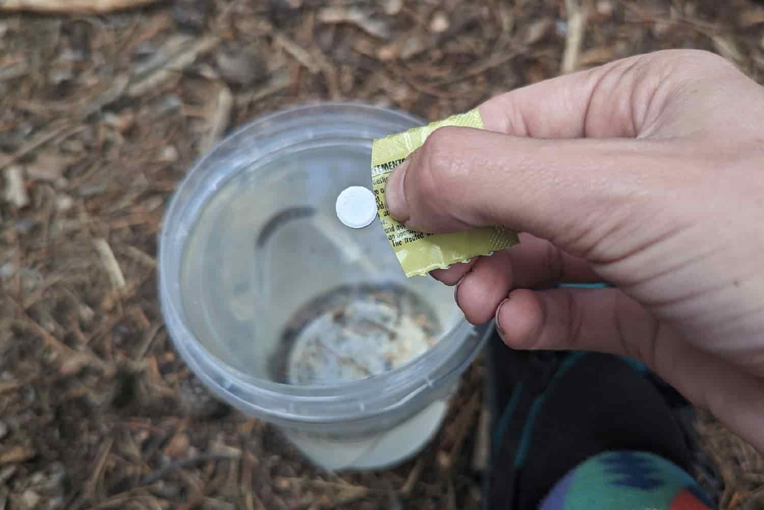 A backpacker dropping a white micropur tablet into a bottle of untreated water