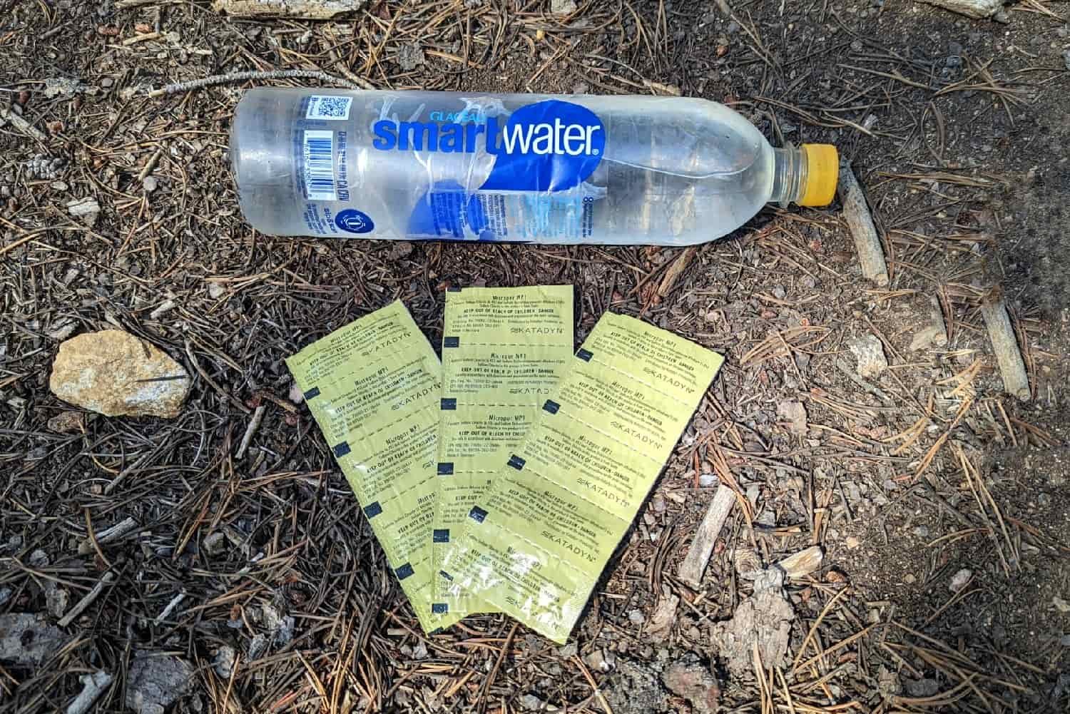 a water bottle and packets of katadyn's micropur water treatment tablets on display on the dirt