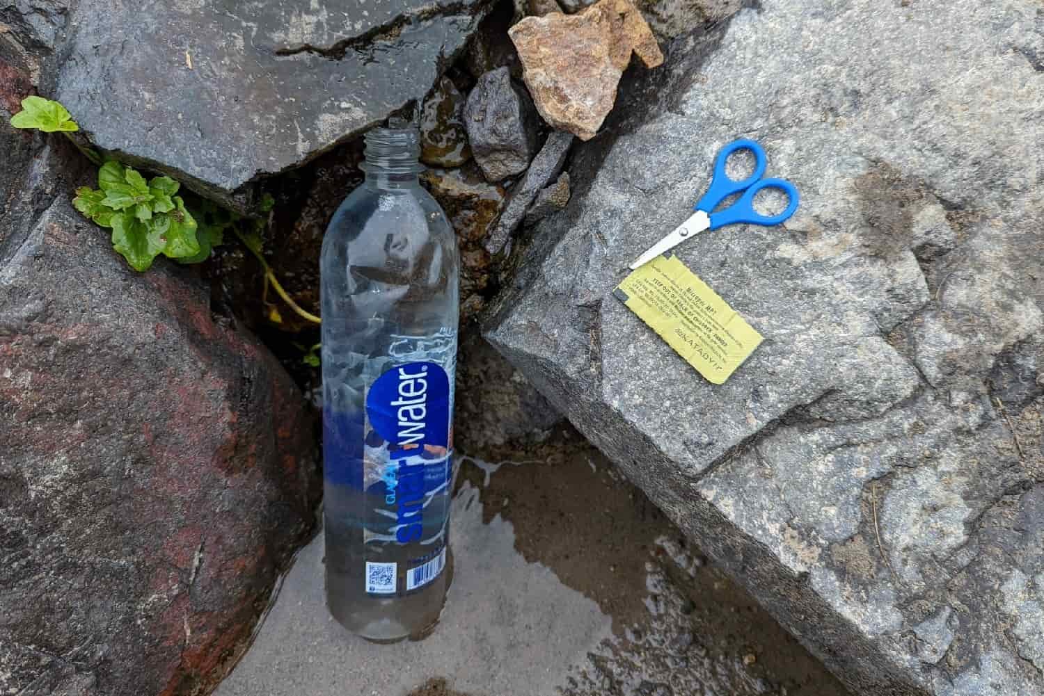 a smart water bottle placed in shallow water with scissors and a micropur tablet in a sealed pouch