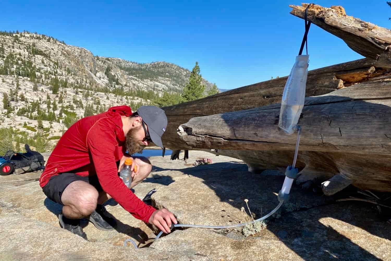 backpacker hangs the dirty reservoir of their gravity fed water treatment system in yosemite to drink clean water while backpacking