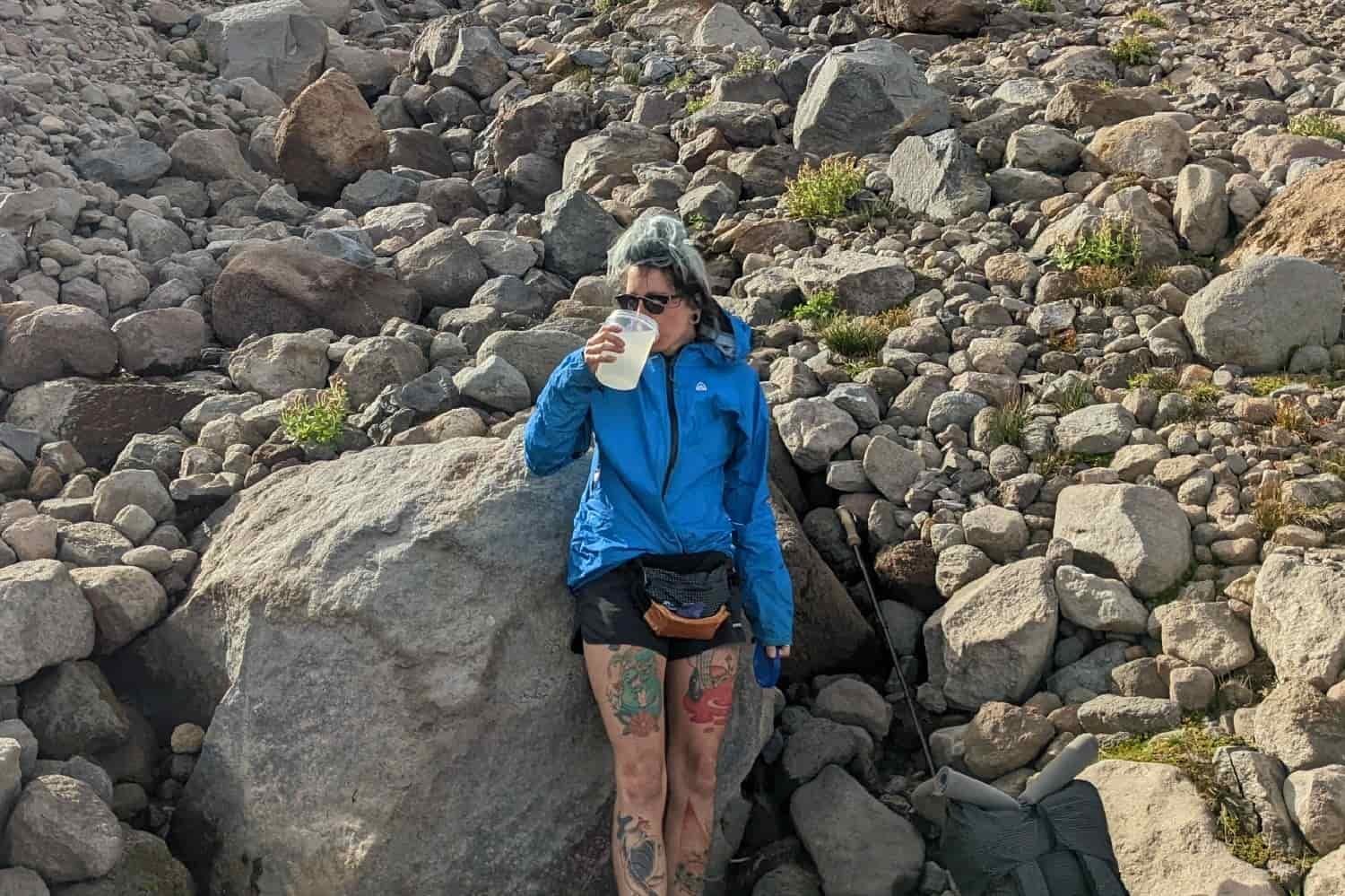 a hiker taking a break in a boulder field drinking water and wearing a zpacks rain jacket