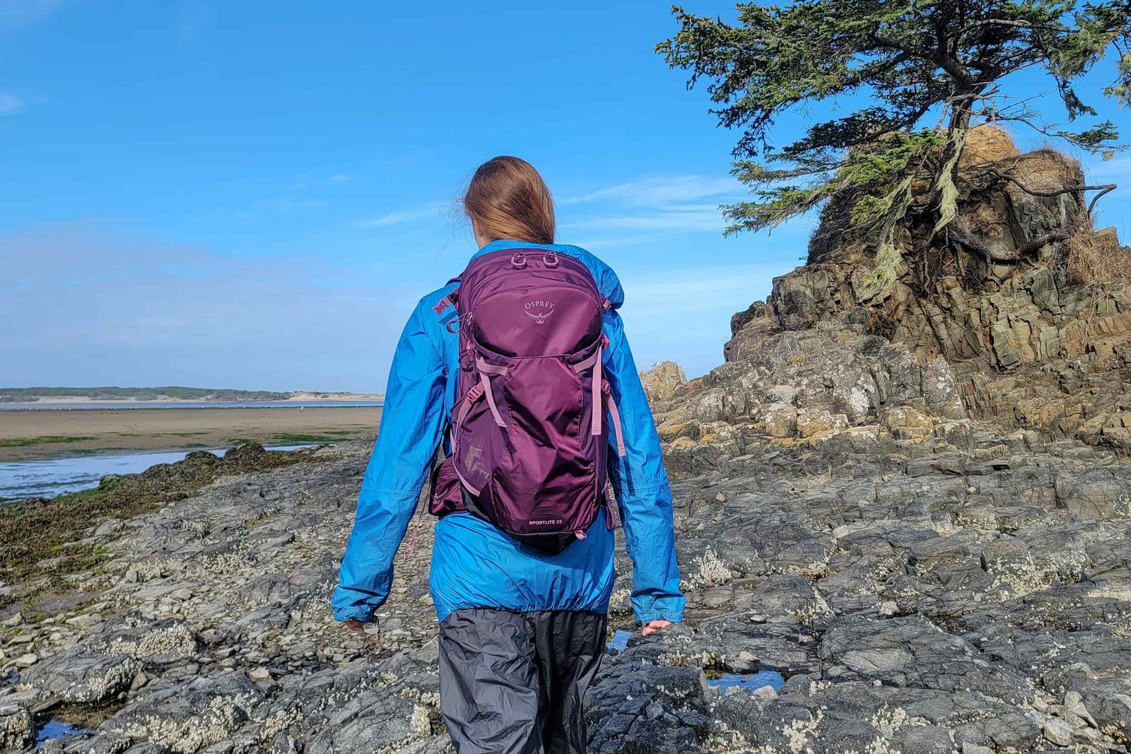 a backpacker walking out onto a shoreline on the pacific ocean wearing a zpacks vertice rainjacket