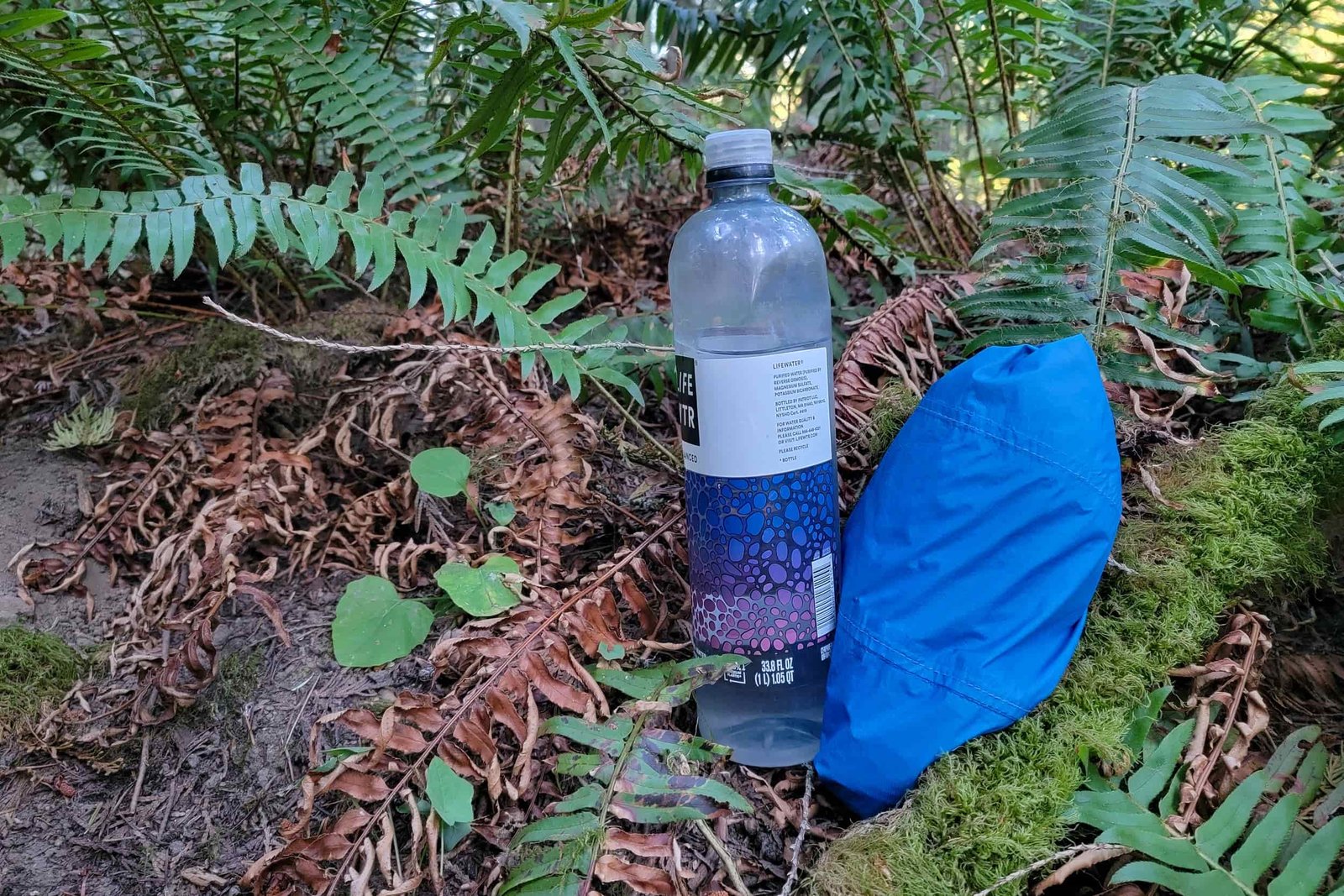 a packed zpacks vertice jacket rolled into the breast pocket on the ground next to a water bottle for size comparison
