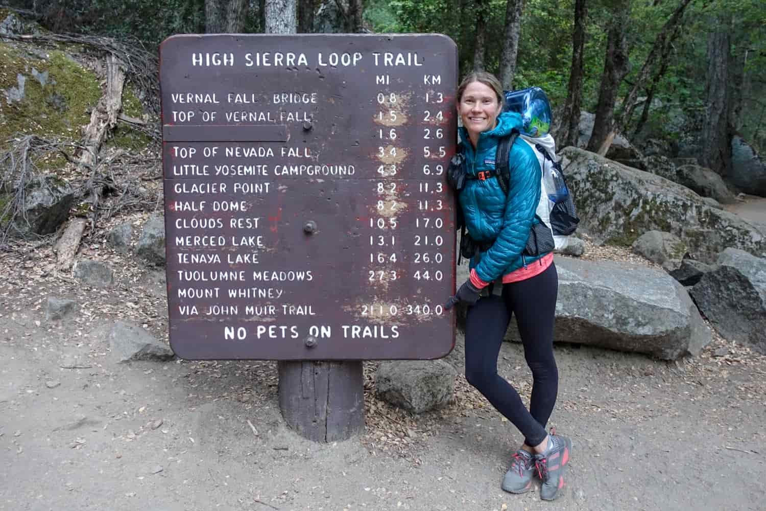 Backpacker pointing to a sign denoting mileage and kilometers for the High Sierra Loop