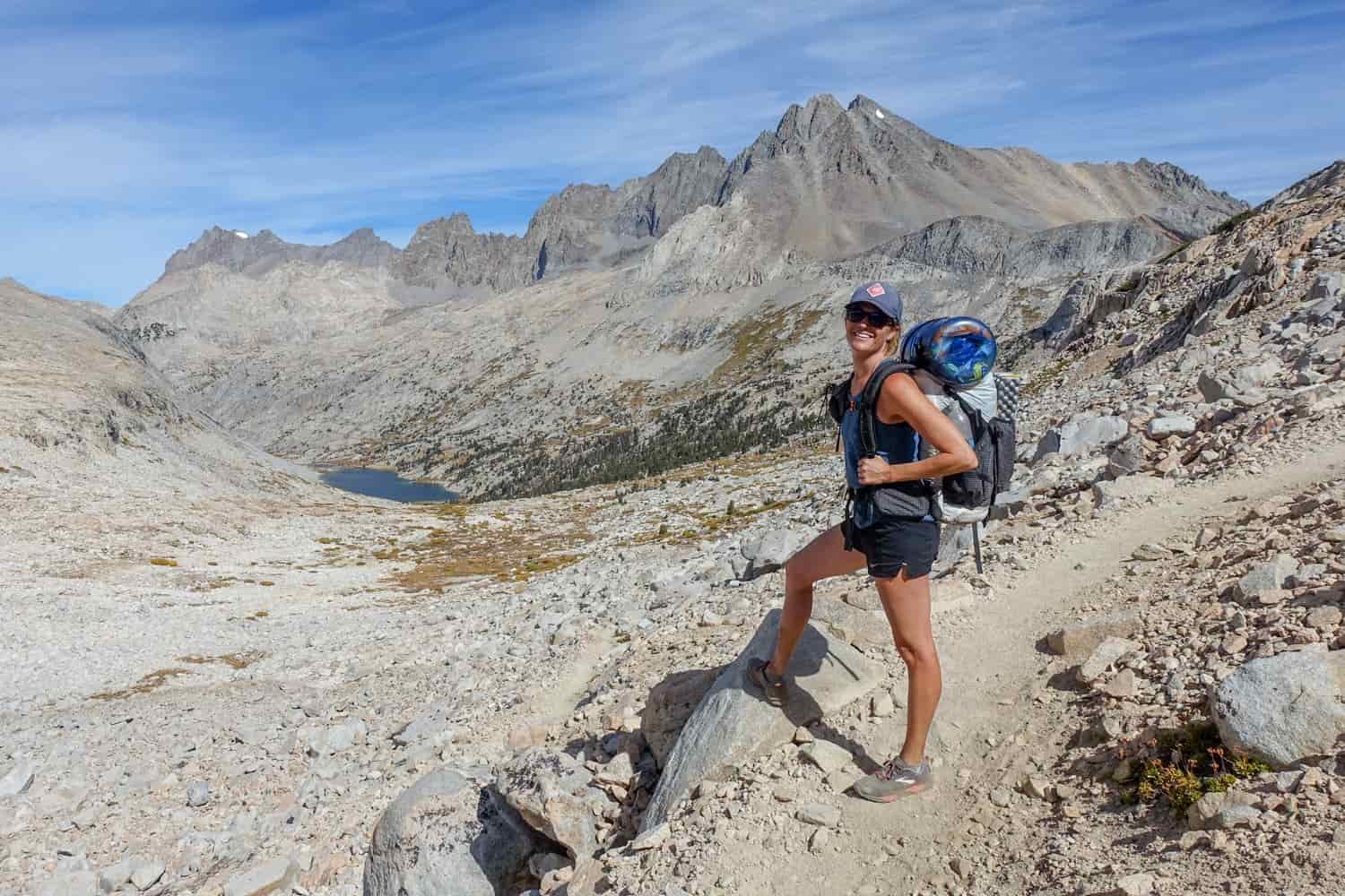 backpacker on the john muir trail posing above a mountain basin and alpine lake in the sun