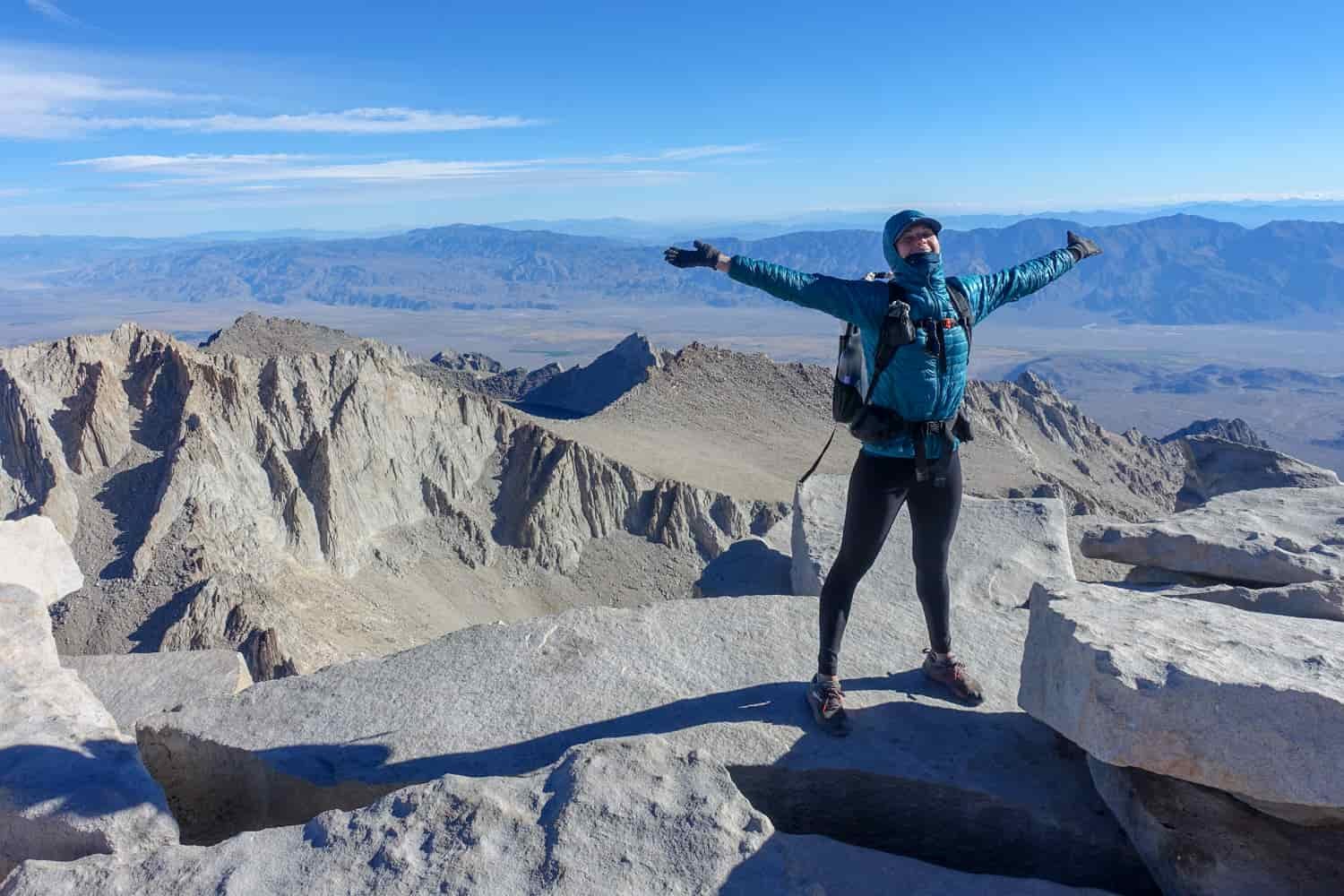 Backpacker celebrates with her hands to the sky on the summit of Mount Whitney.