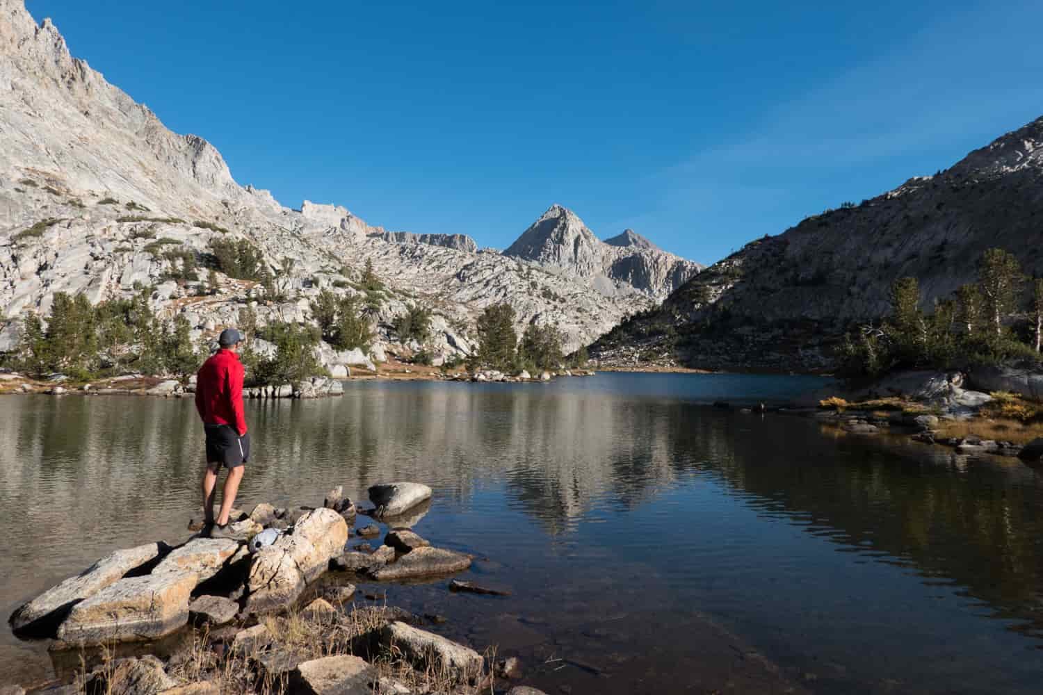 Backpacker stepping out on a rock in a lake with white granite mountains surrounding.