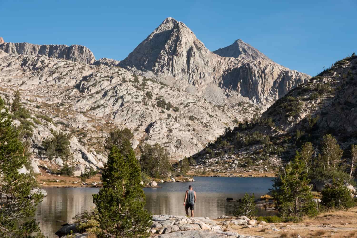 backpacker taking a break and walking into an alpine lake on a sunny day.