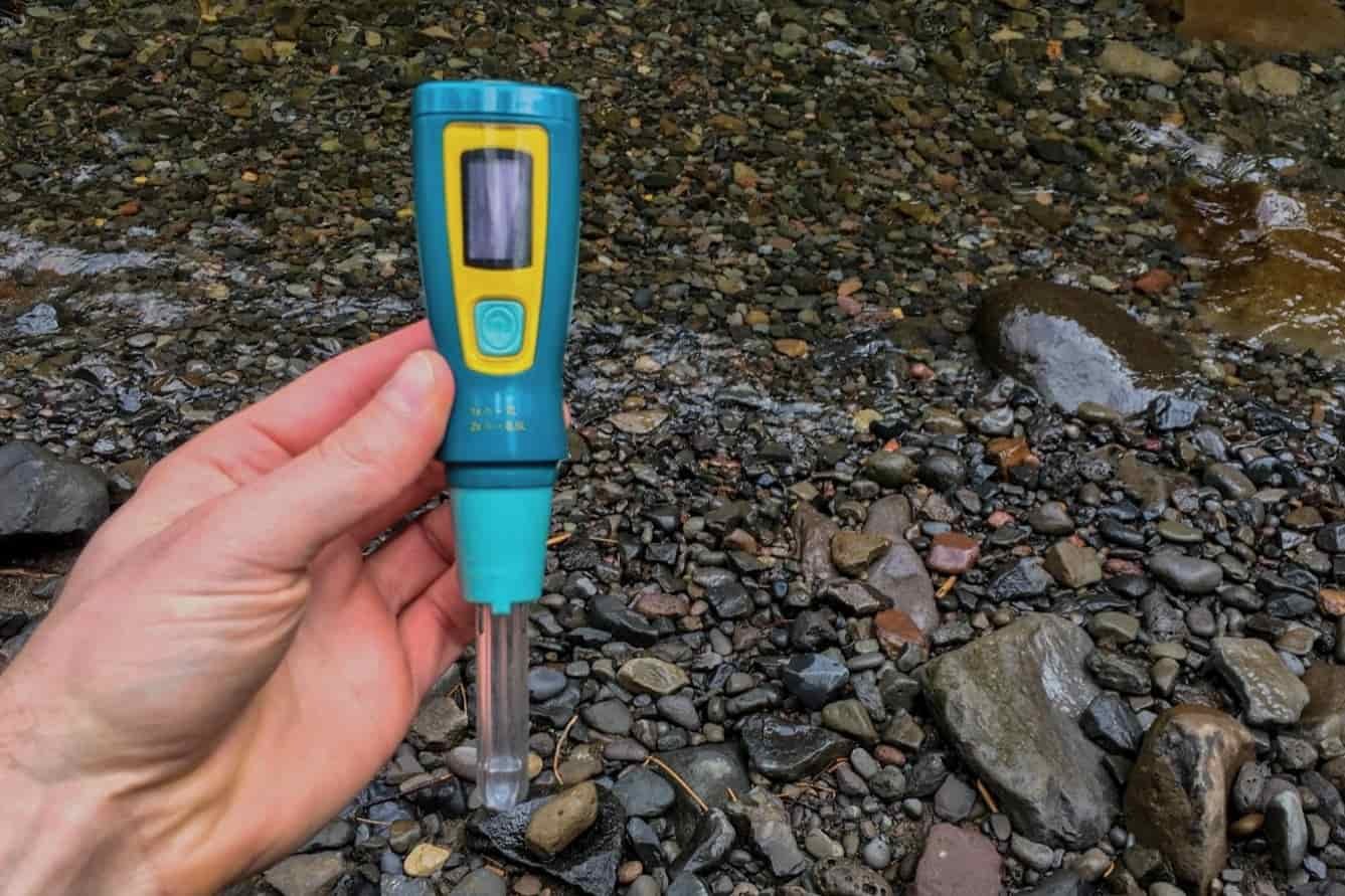 a hand holding the steripen over river rocks