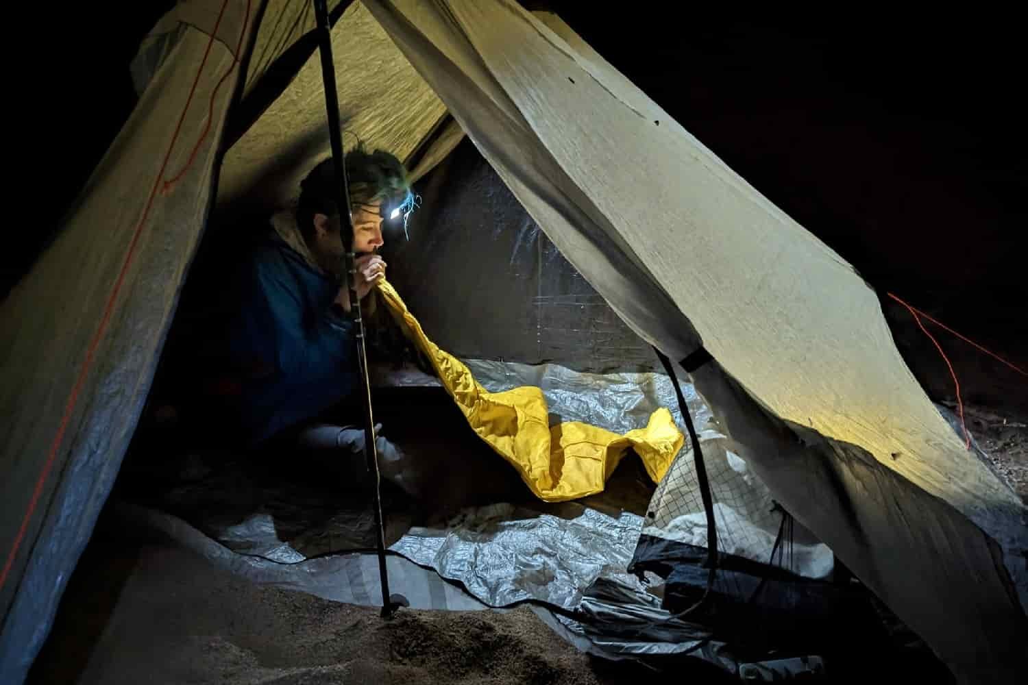 a thru-hiker inside their tent at night inflating their therm-a-rest neo air xlite nxt sleeping pad. The scene is lit up with a headlamp