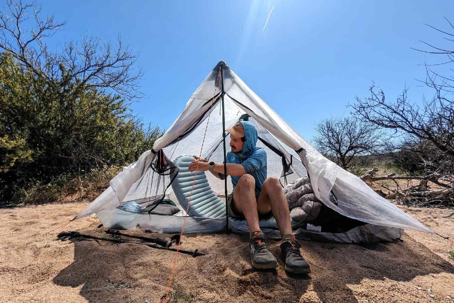a thru-hiker holds their therm-a-rest while seated inside their tent on a sunny day in the desert