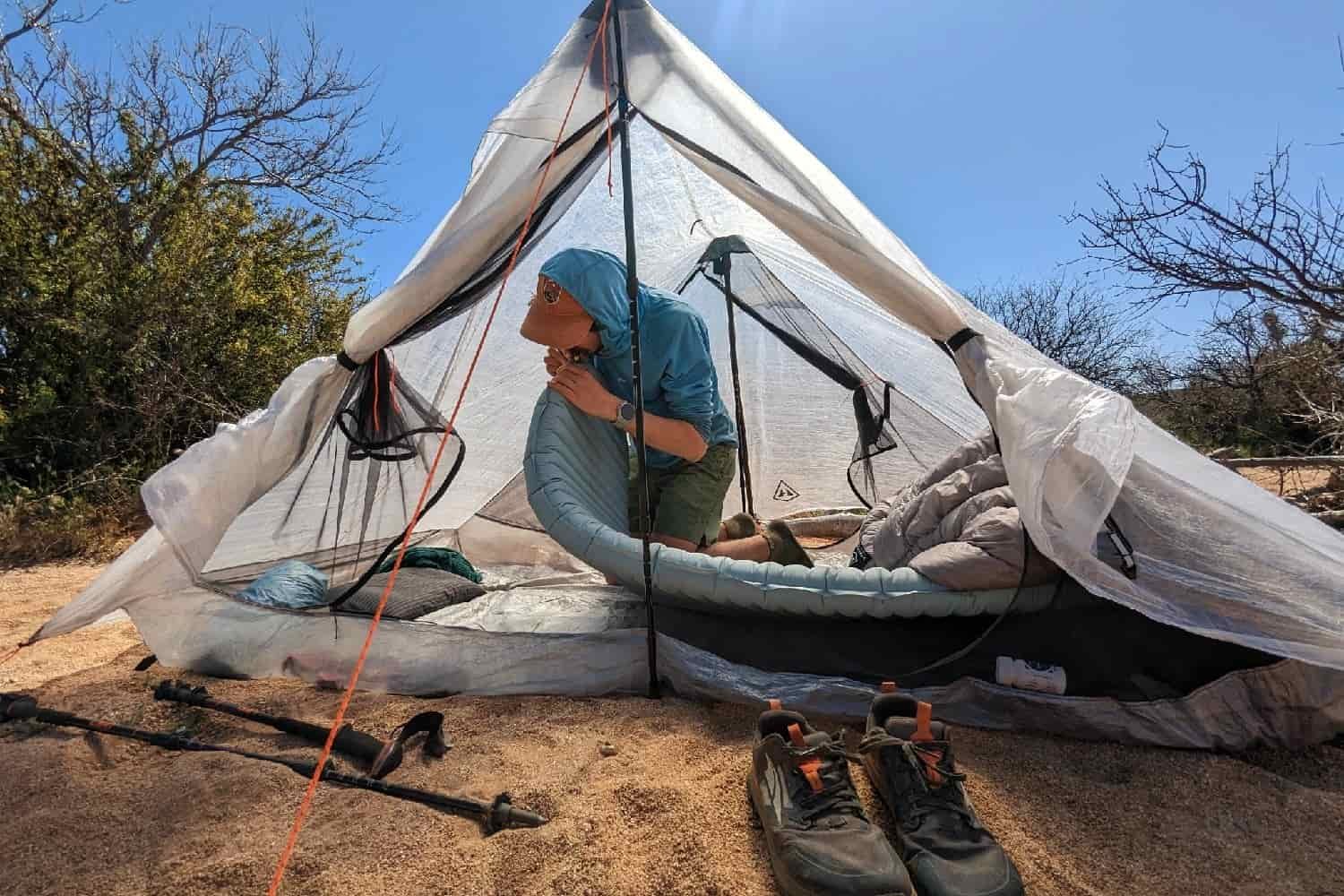 a thru-hiker in the desert puts their mouth to the valve of the NeoAir Xtherm NXT to add more air to increase its firmness while inside their tent on a sunny day