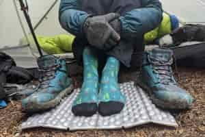 A backpacker sitting in a tent wearing Smartwool PhD Outdoor Light Crew Socks, the socks are patterned and blue