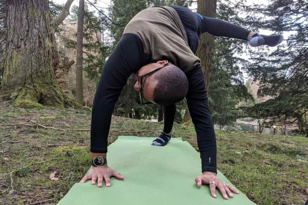 A male holds a yoga pose on a mat on a green hillside