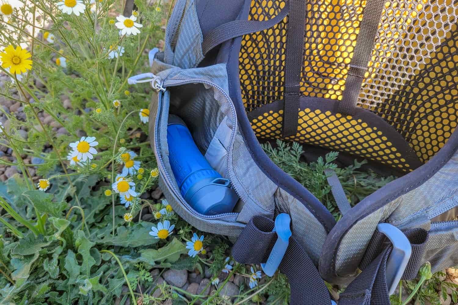 the quickdraw filter in an unzipped hipbelt pocket on a backpack with flowers on the ground surrounding it