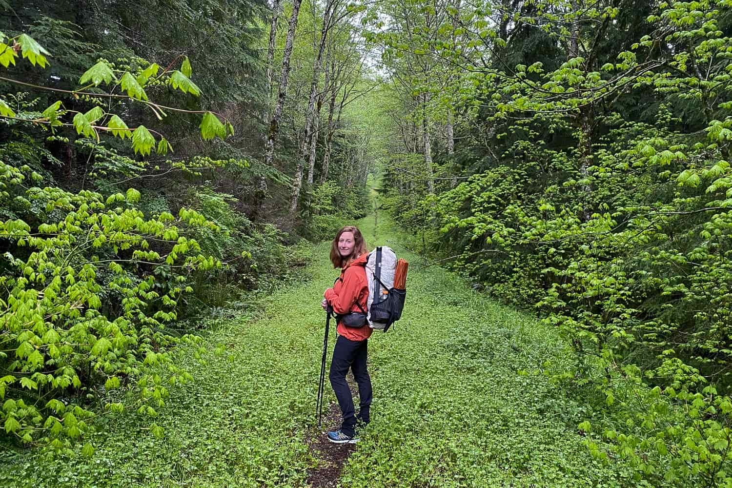 a women stands in the middle of a foliage heavy forest and looks at the camera