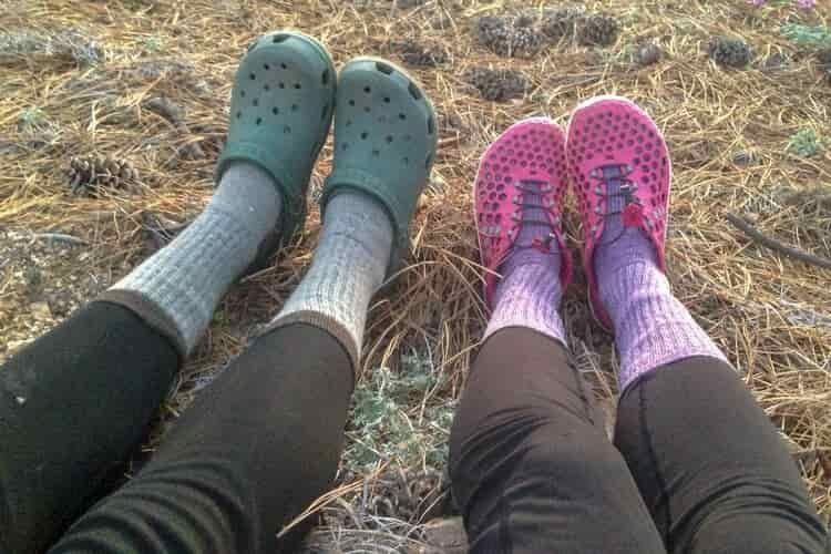 Lower body shot of two female hikers at camp wearing leggings, fresh hiking socks, and colorful crocs on their feet