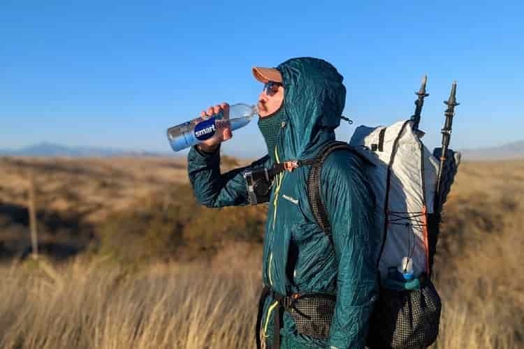 A male hiker sips water from a bottle while covered in lightweight layered clothing 