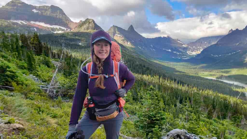 A female backpacker wearing the Eddie Bauer Super Sevens Fleece Pullover in front of jagged mountain peaks in Glacier National Park
