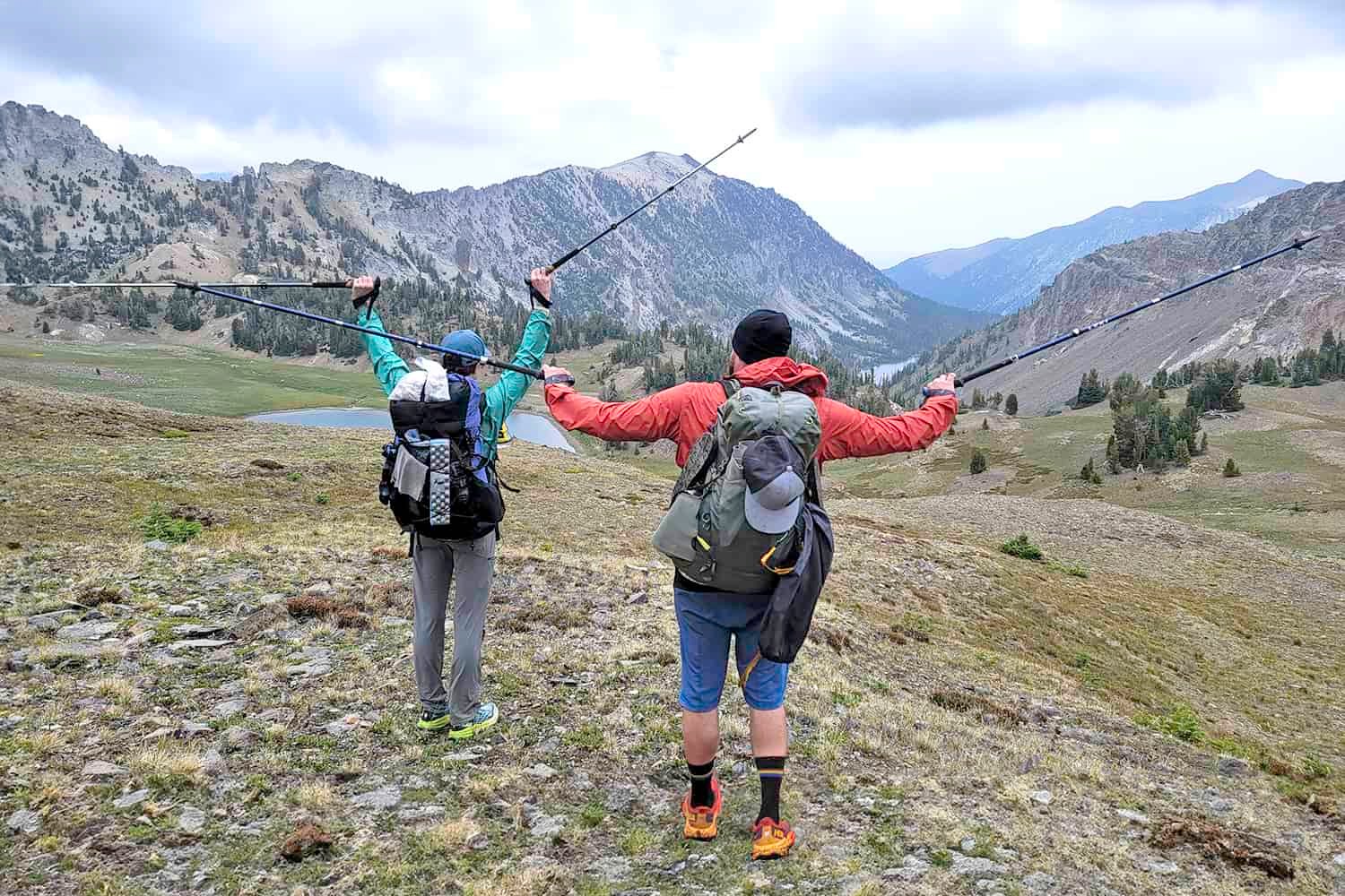 Hikers holding their Black Diamond Pursuit and LEKI Makalu Lite trekking poles up in the air while looking out over an expansive view of mountains and lakes