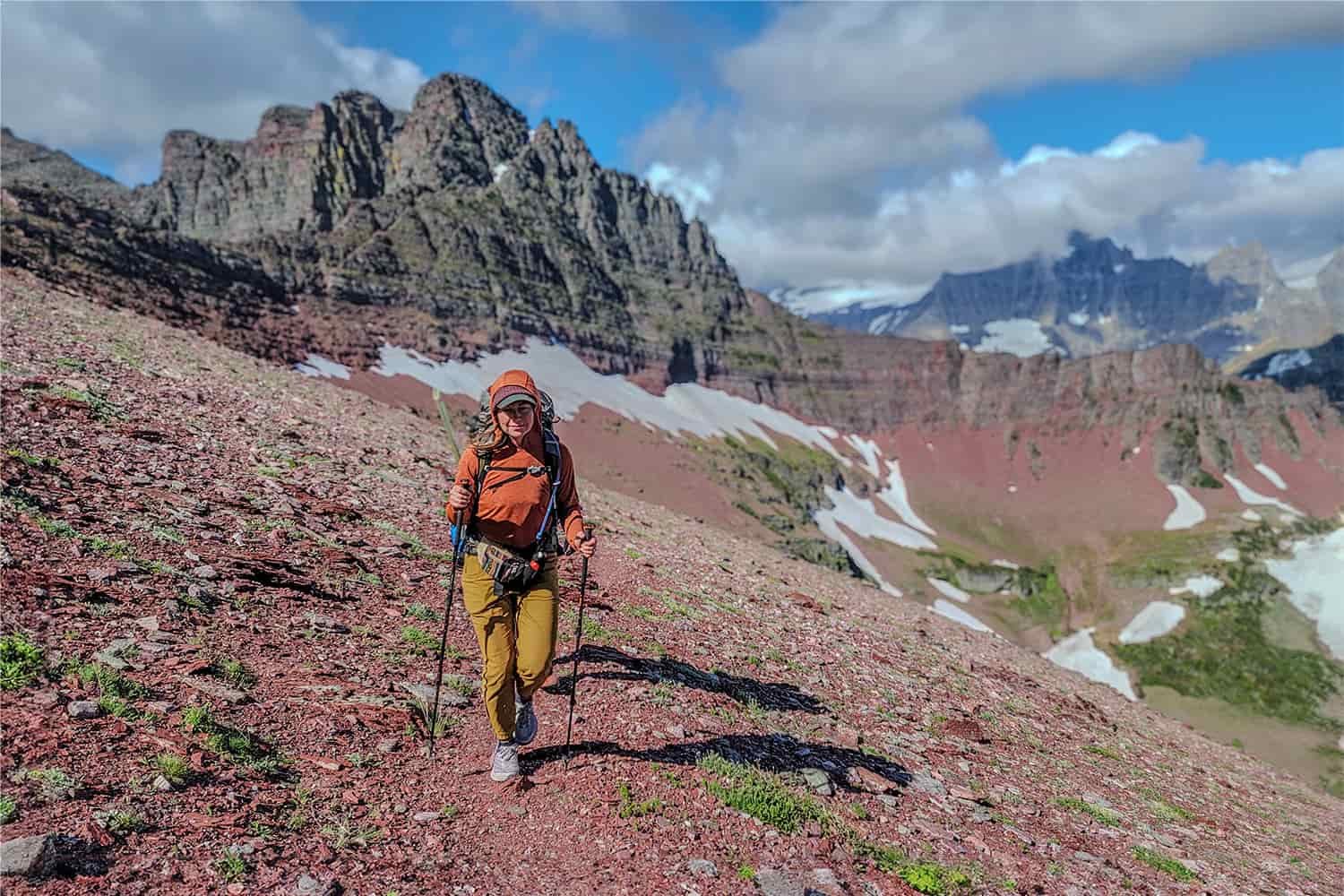 A female backpacker hiking up to the top of a red, rocky mountain pass in Glacier National Park using the REI Flash Carbon trekking poles