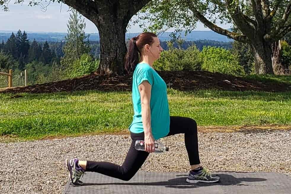 A woman does lunges outdoors with water bottles in her hands for added weight