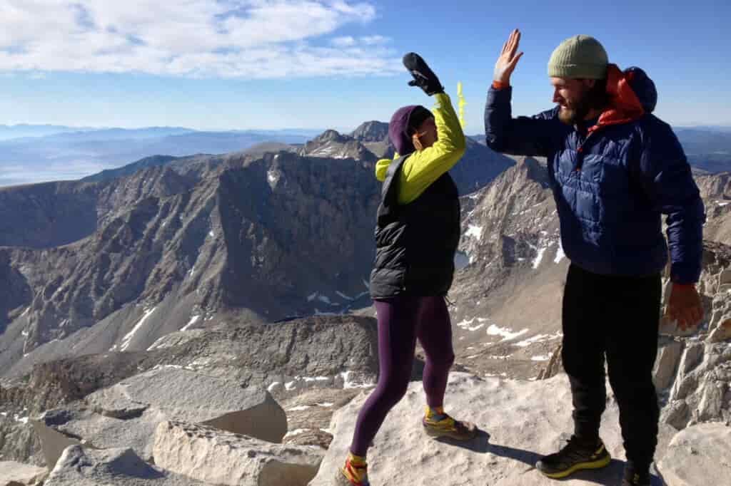 A male and female hiker give each other a high five at a high point on their hiking route