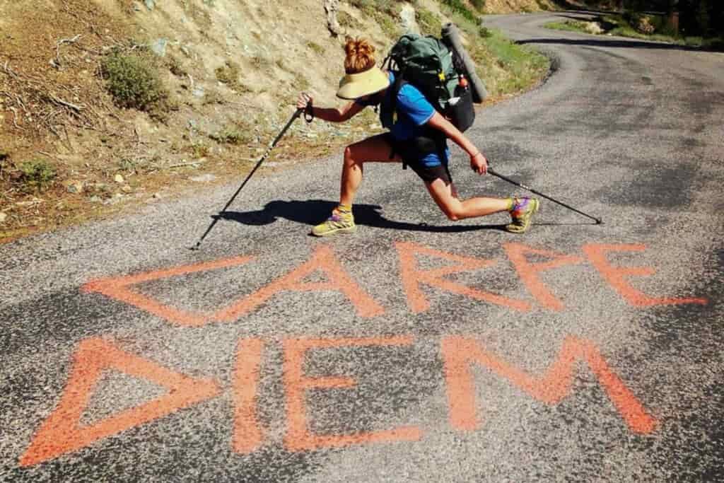A hiker poses on a road behind the spray-painted words "carpe diem"