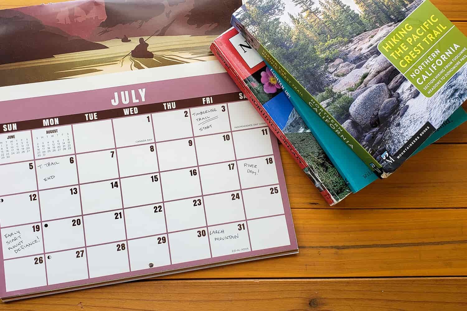A calendar lays next to hiking guide books on a wooden table