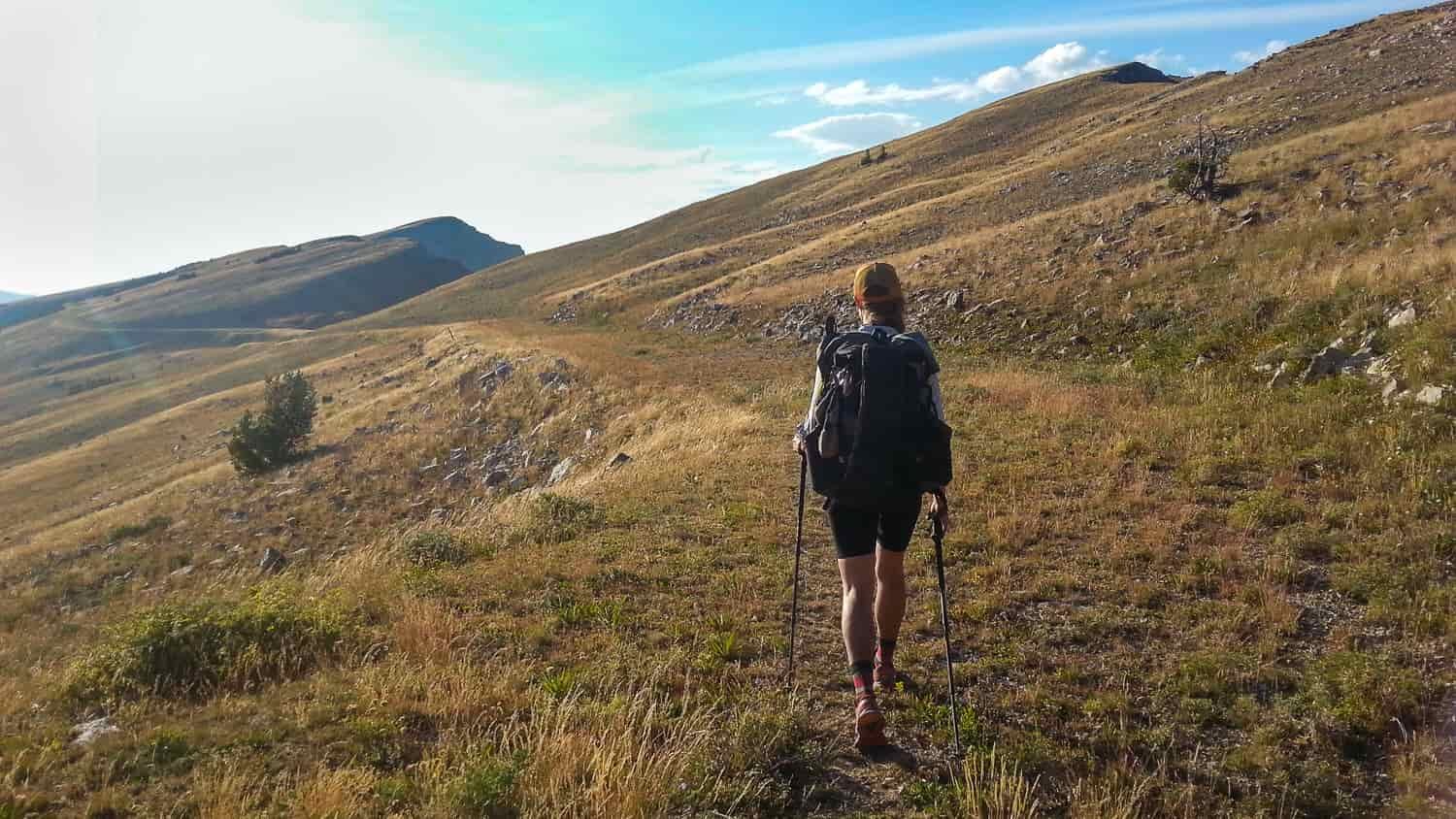 A fit, female hiker walks down a grassy trail in the mountains