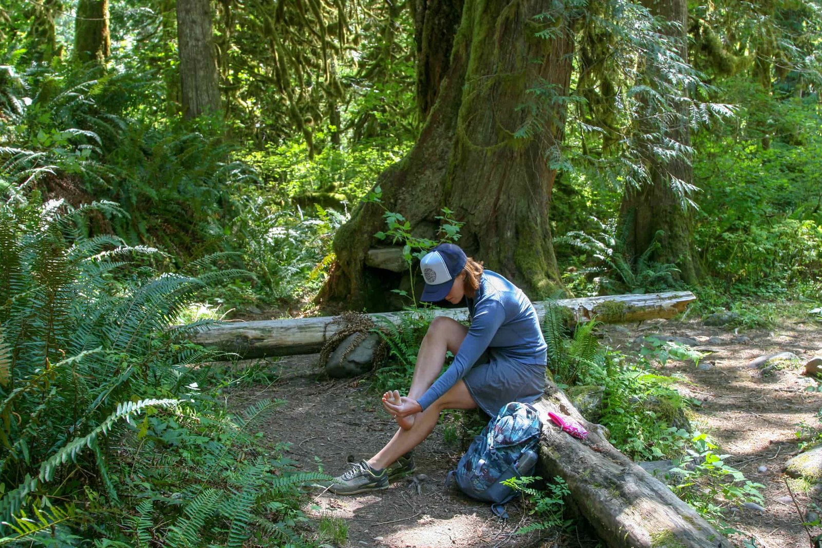 A woman sits on a log along the trail, examining a blister on her foot