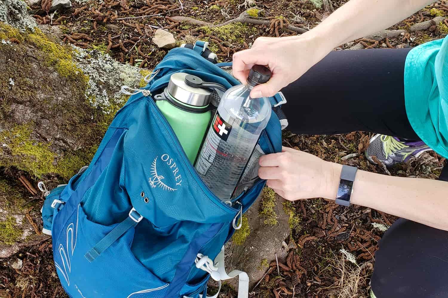 A blue Osprey daypack with two full water bottles inside