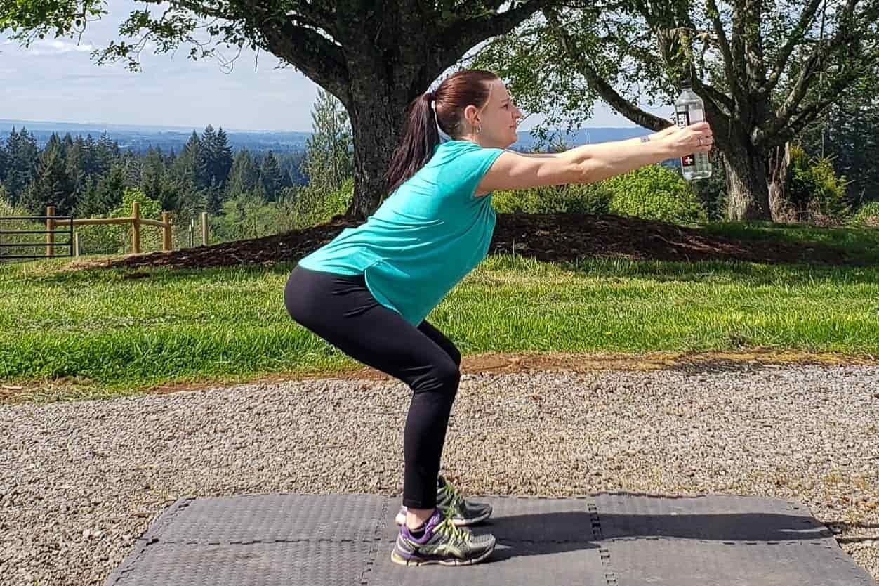 A woman does squats on a mat on a gravel lot outdoors