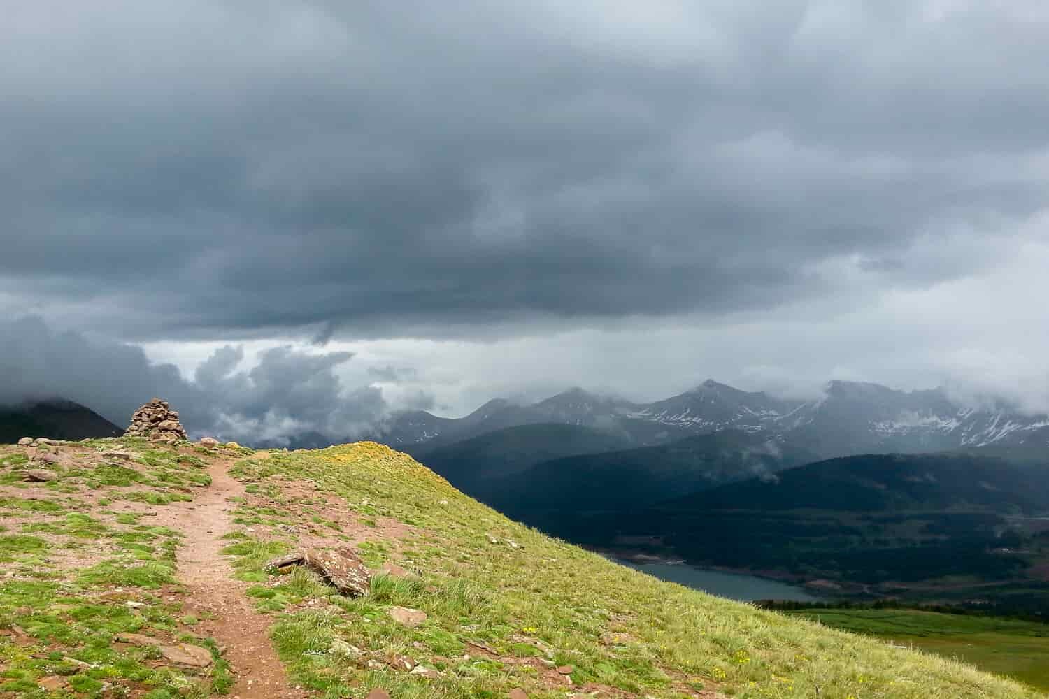 trail leading to a rock cairn with storm clouds overhead