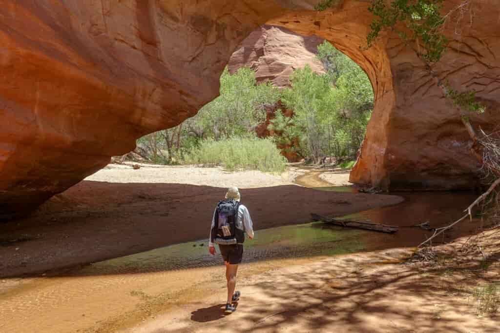 a man wtih a small backpack walks away frm the camera through a rock arch