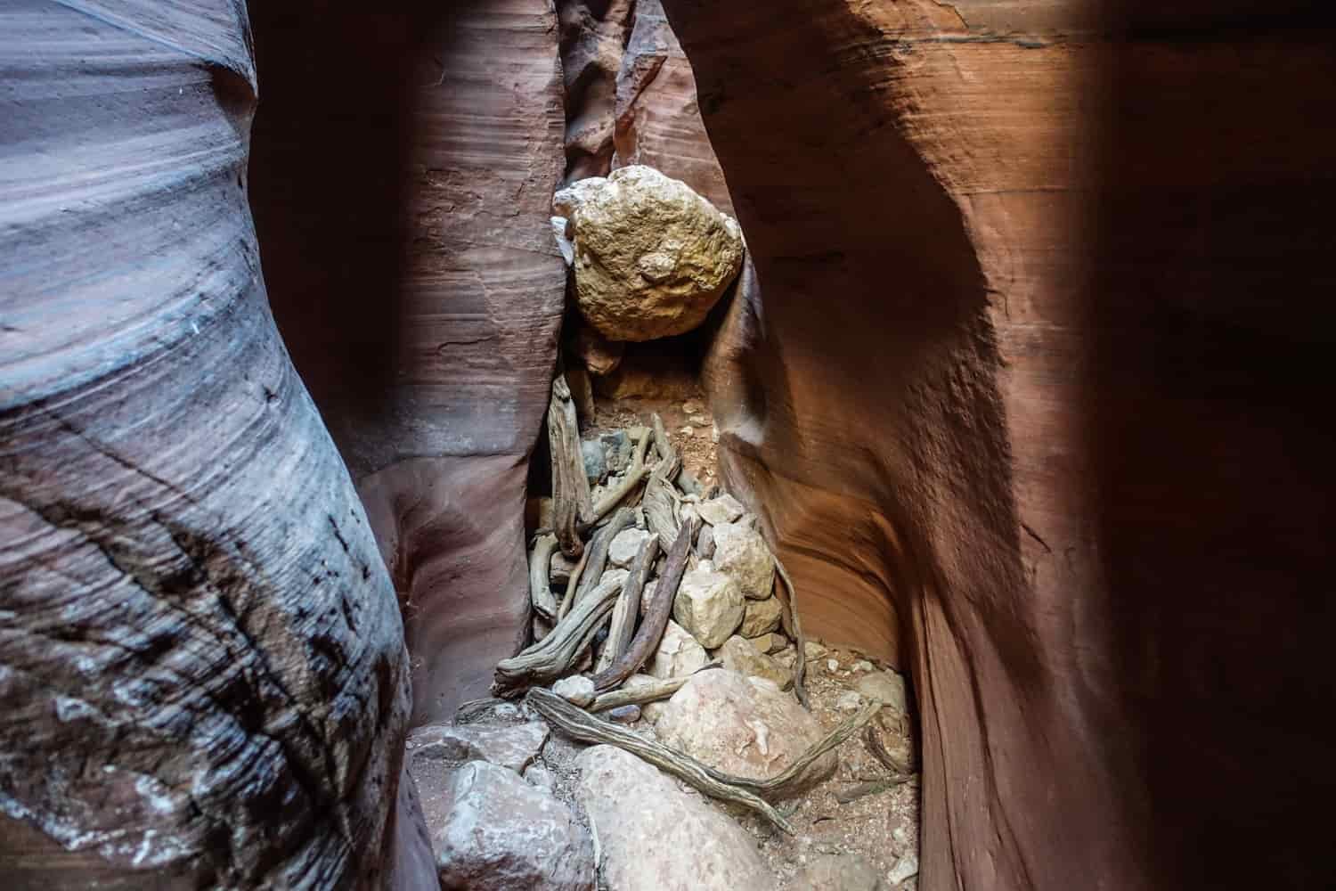rocks suspended and lodged in narrow slot of a canyon showing how the rainfall once could move rocks and logs.