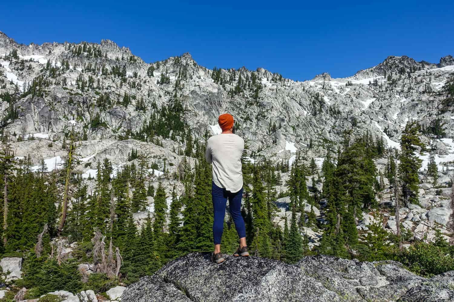 backpacker in his base layers looking a basin of granite and snow on a sunny day in the trinity alps