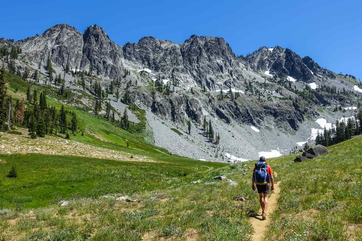 backpacker in the trinity alps walking toward a craggy granite ridge on a sunny day