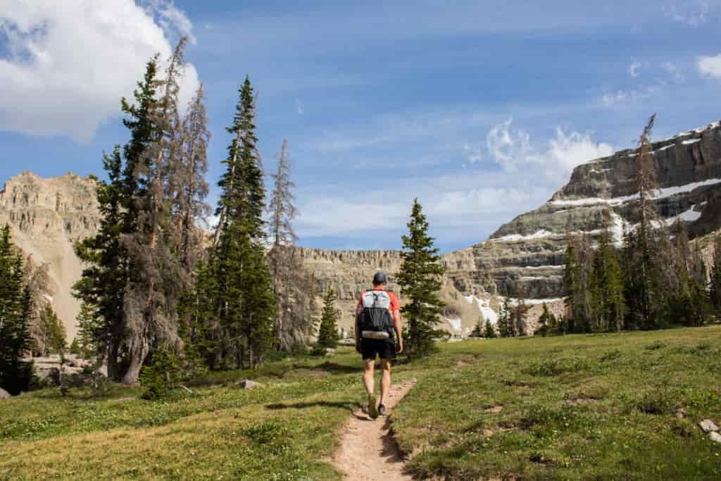 A backpacker in shorts walks down a trail wearing a lightweight backpack