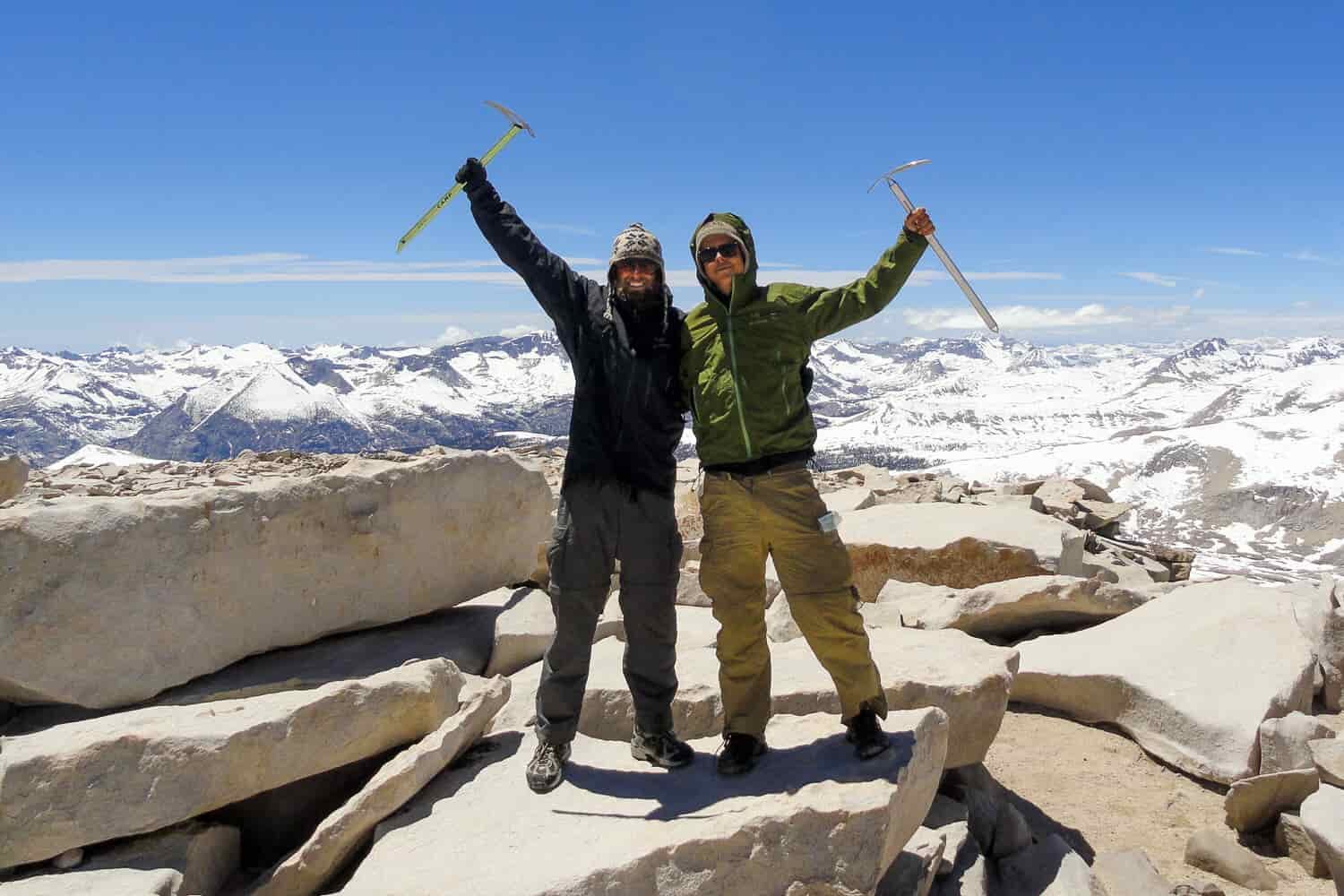 Hikers pose for a picture on top of a mountain with their ice axes raised