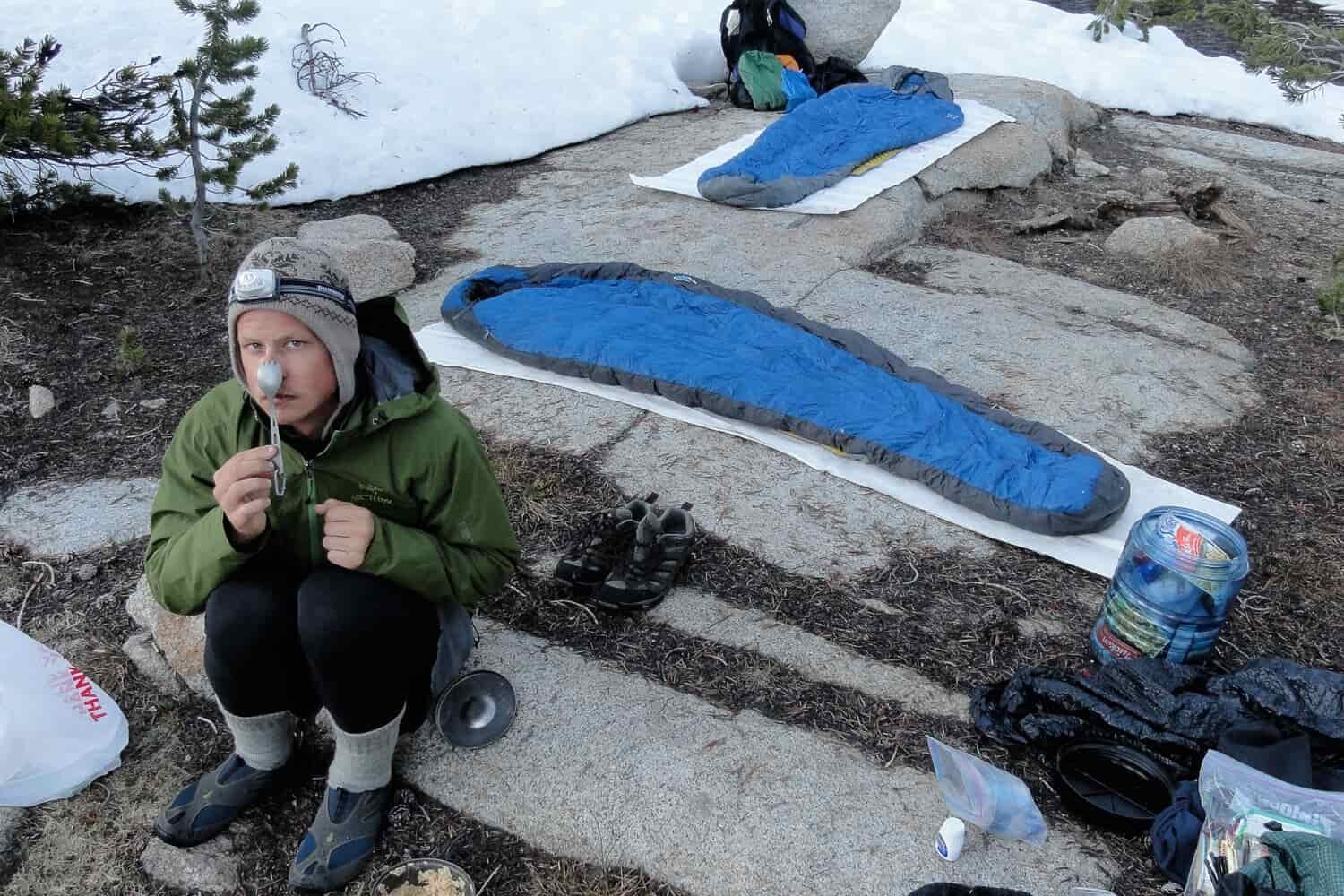 hiker seated at his campsite with sleeping bags on the rocks