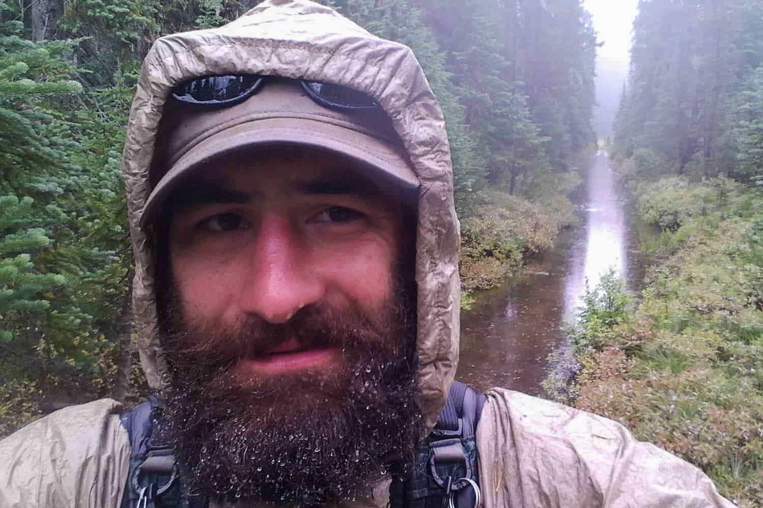 Thru-hiker posing for a picture on a trail covered in water in the rain