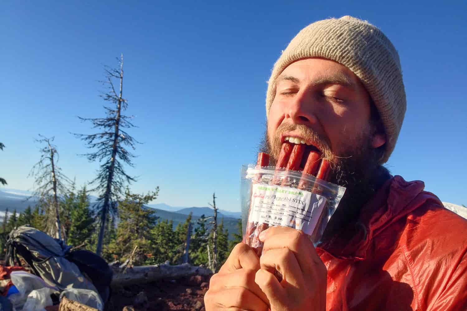thru-hiker eating meat jerky on a sunny vista.