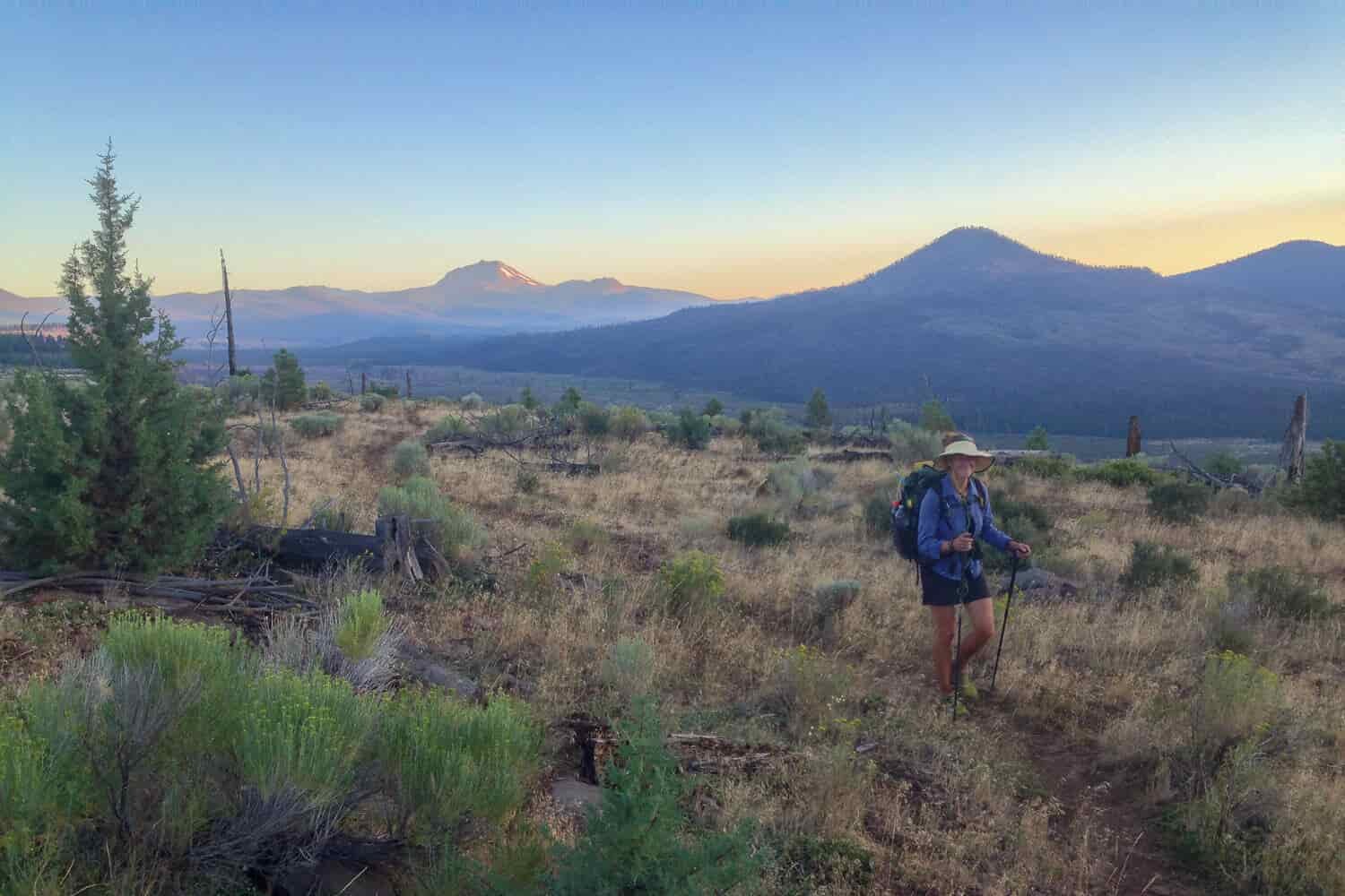 thru-hiker walking during sunset on a open meadow with blue and orange skies.
