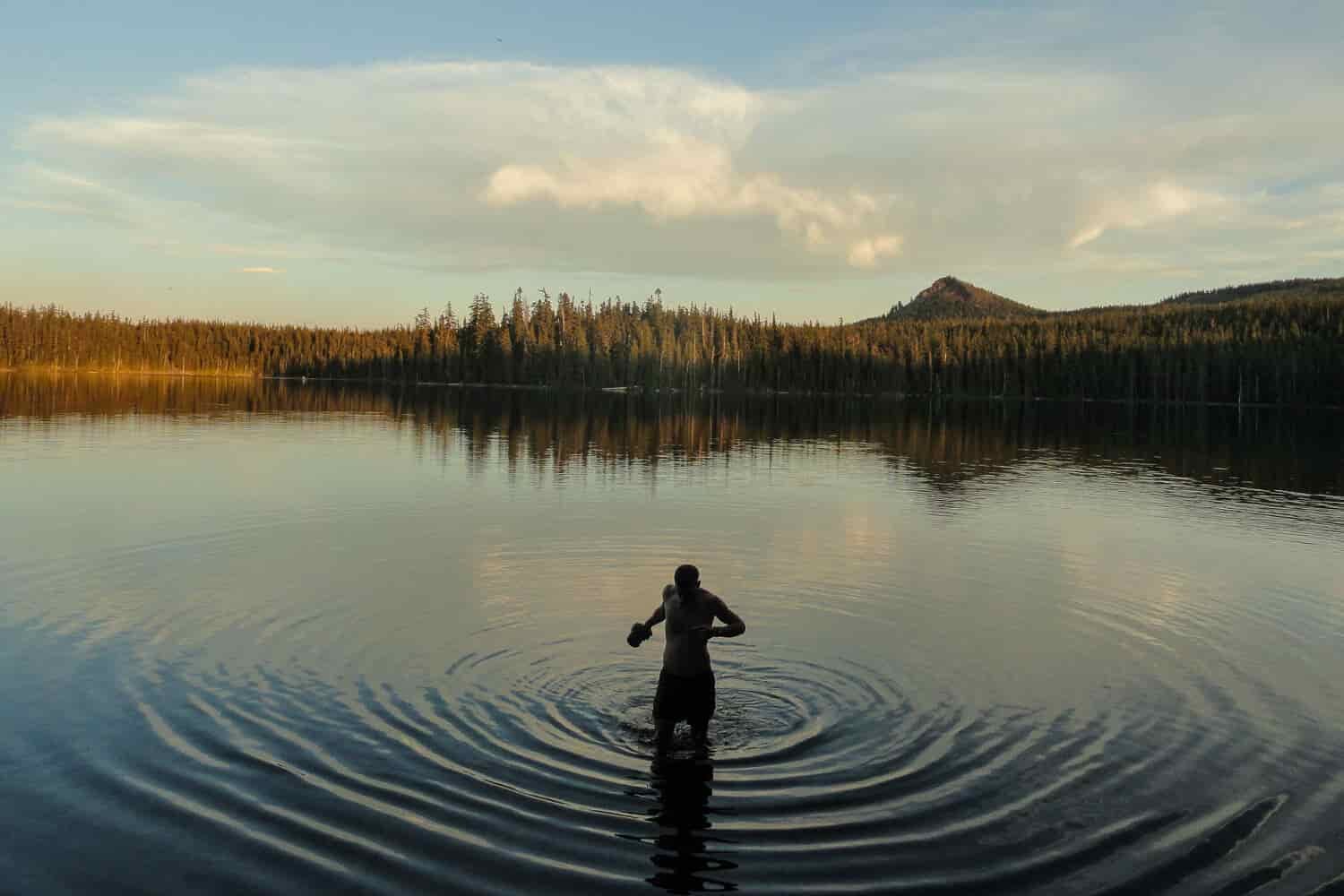 thru-hiker taking a dip in a still lake.
