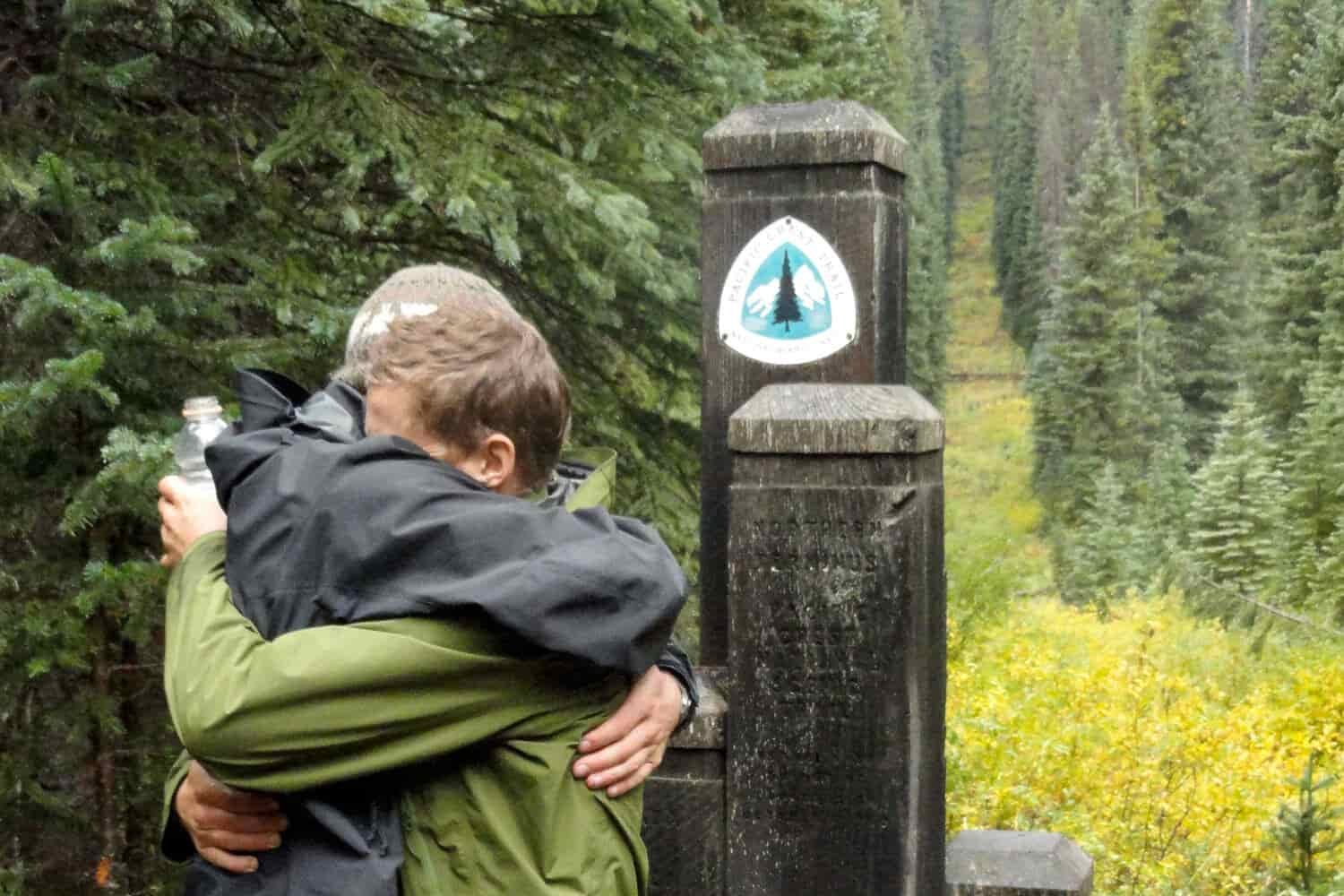thru-hikers embrace in a hug at the northern terminus of the PCT in the fall