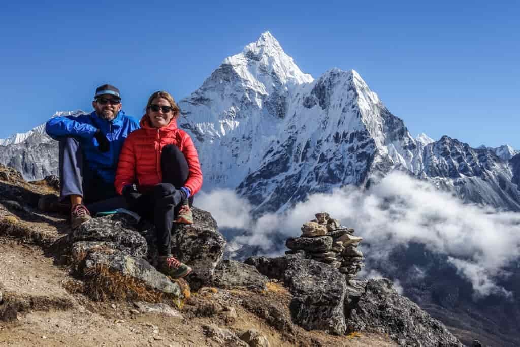 Two backpackers pose in front of a giant mountain covered in snow 