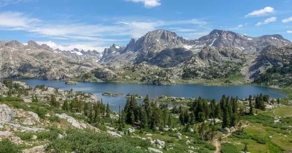 a sweeping view of a lake with small islands in it surrounded by granite peaks on a sunny day