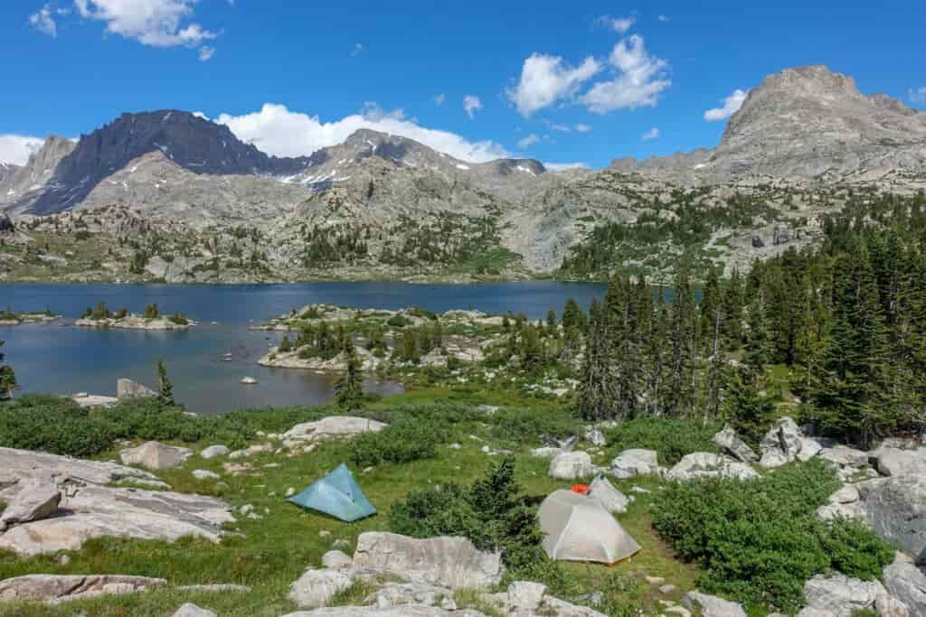 two tents pitched in a green meadow above a lake in the wind river range