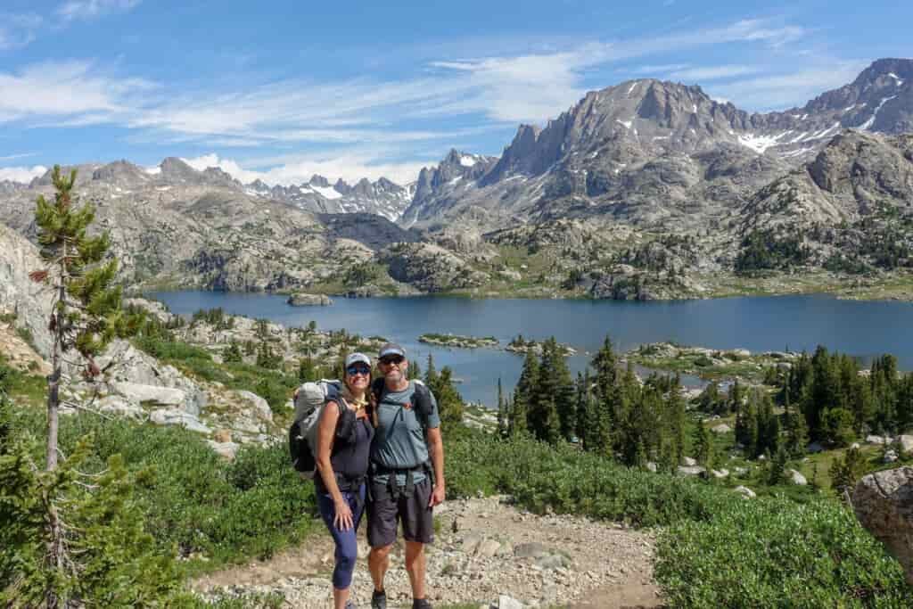 two backpackers posing above a lake with islands in it and mountains surrounding the lake